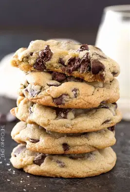 A sack of five salted chocolate chip cookies on a table with sligtly blurred salt and a salt shaker in the background.